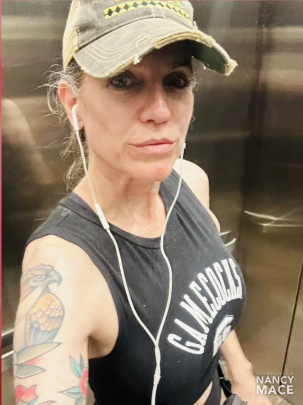 Close-up of Nancy Mace in an elevator wearing a Gamecocks tank, her upper arm showing a color hawk tattoo with orange and grey, and traditional-style work continuing down the forearm.