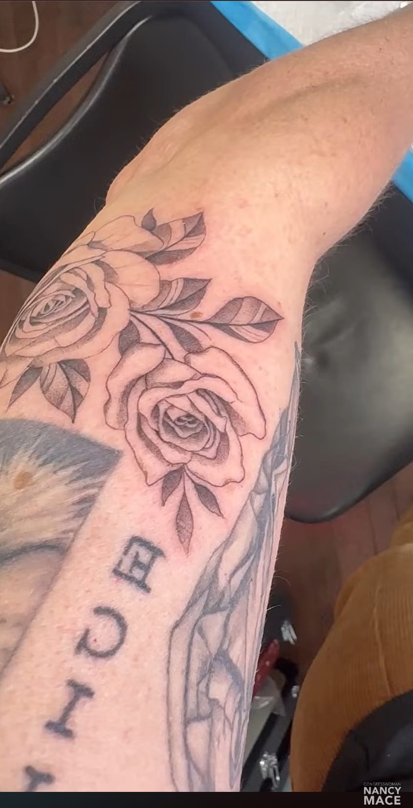 Close-up of Nancy Mace’s forearm showing two large black-and-grey rose tattoos with leaves, above the vertical block word JUSTICE and additional line work.