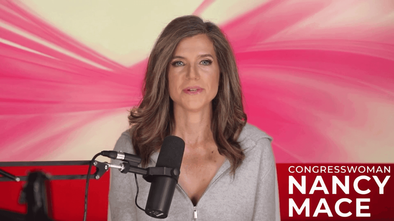 Still: Mace at a boom microphone in front of a red-and-pink studio backdrop