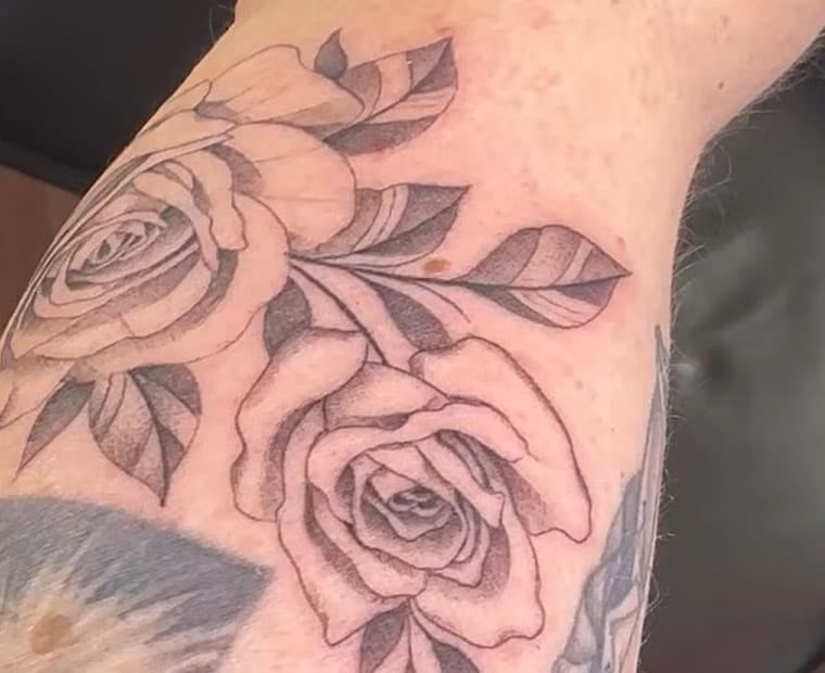 Close-up of a pair of large fine-line black-and-grey rose tattoos with leaves on Nancy Mace's left forearm.